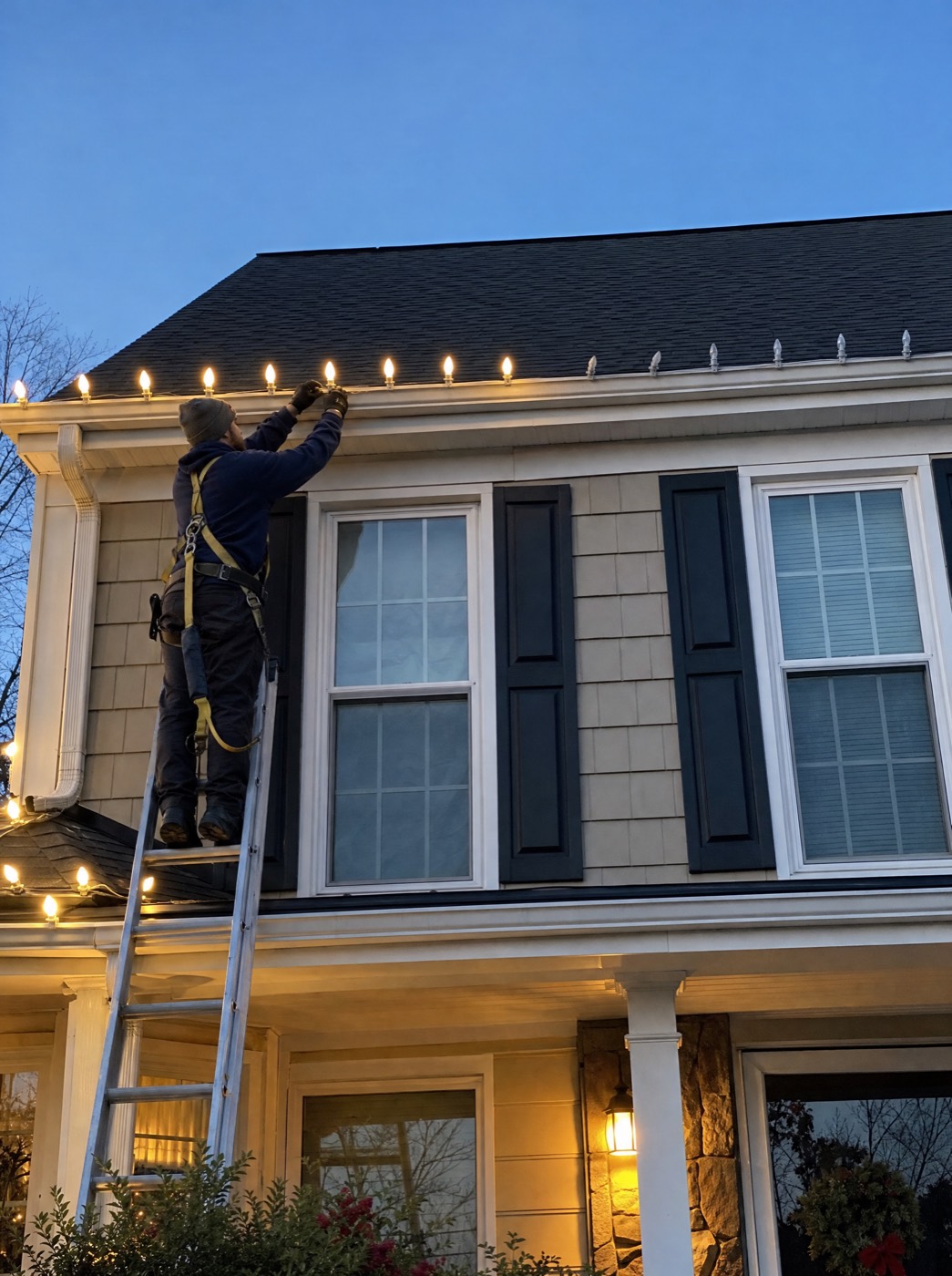 Installer in a safety harness clipping bulbs to a gutter at dusk