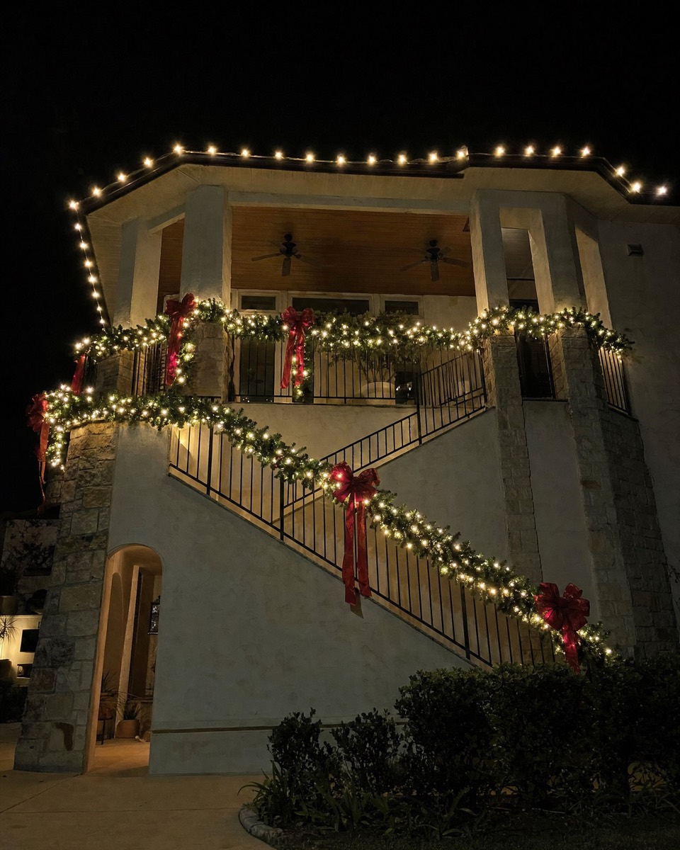 Balcony and stair railings wrapped in lit garland with red bows